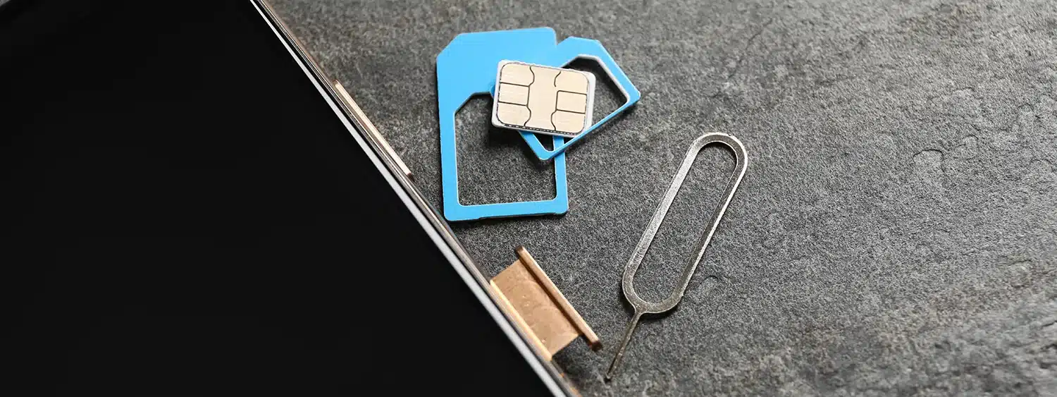 Nano-SIM, adapters and ejector tool beside smartphone – switching physical SIMs vs using a multi-network SIM